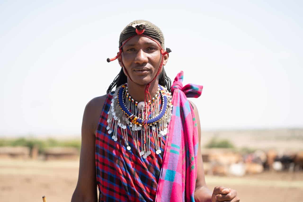 Maasai woman wearing traditional jewelry and clothing in rural setting.